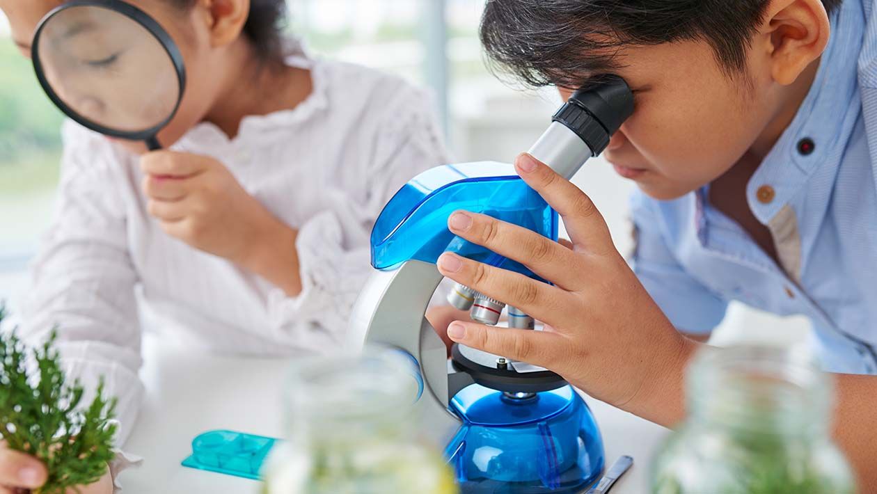 A boy looking through a microscope and a girl looking through a magnifying glass
