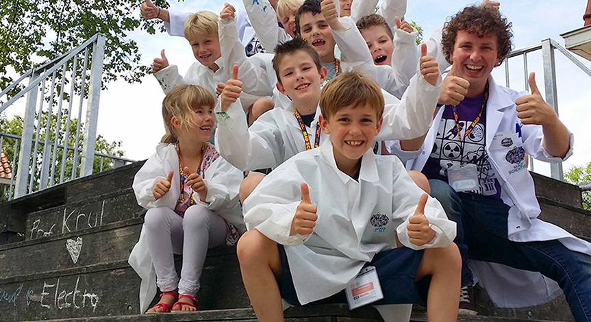 Kids wearing mad science lab coats sitting outside with a mad scientist with their thumbs up
