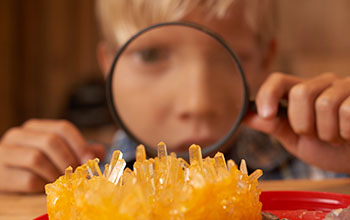 Boy looking through a magnifying glass examines an orange crystal structure